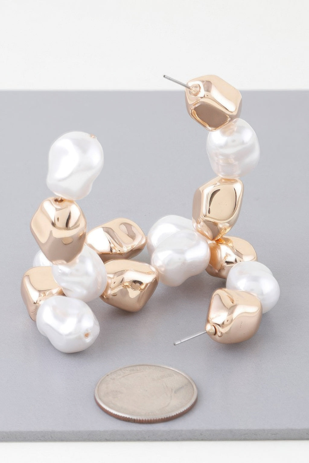 Close-up of shiny N Pearl hoop earrings: white pearls on gold-tone curved bezels