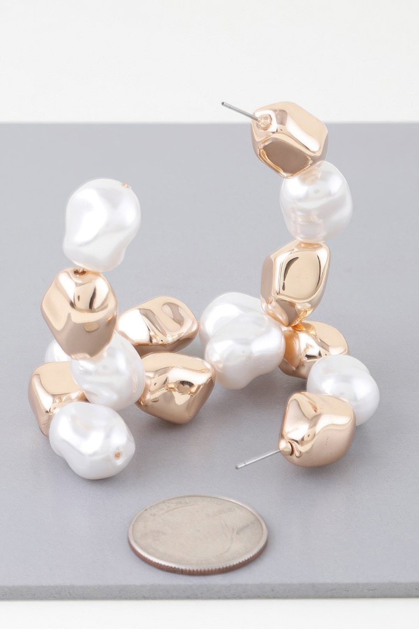 Close-up of shiny N Pearl hoop earrings: white pearls on gold-tone curved bezels