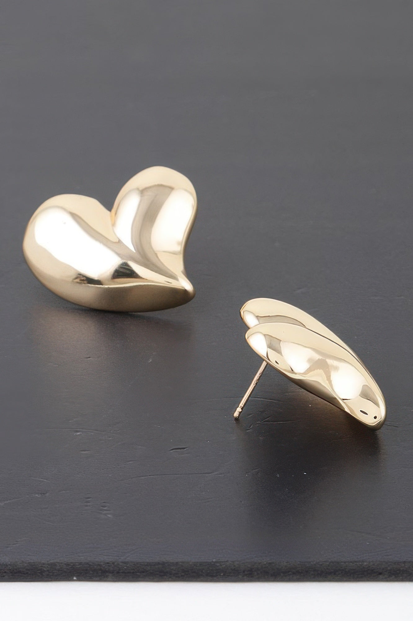Gold twin heart earrings with mirror finish, one angled showing straight post