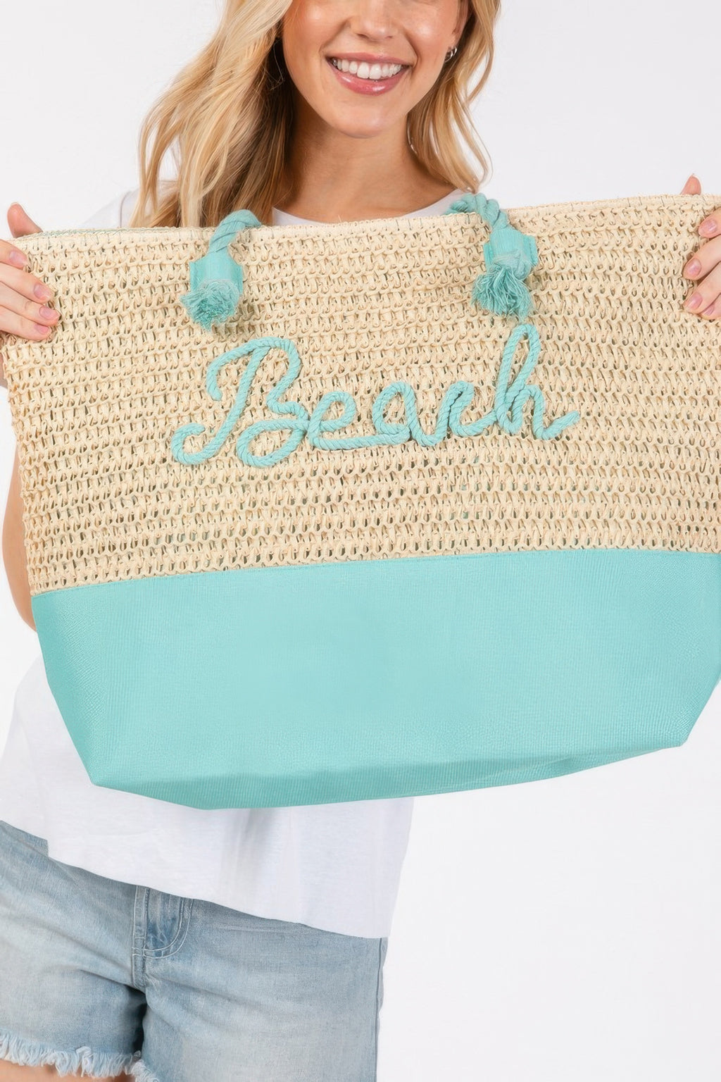 Close-up crochet beach tote, beige knit with teal bottom, rope tassel handles, “Beach”
