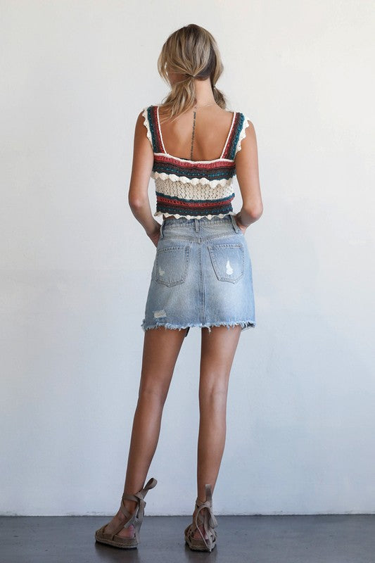 Back view: light wash denim skirt with distressed rips and raw hem edges
