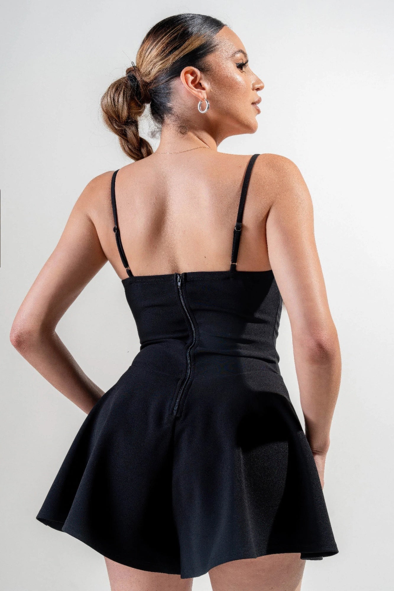 Back view of black stretch woven jumpsuit with thin straps and flared skater hem