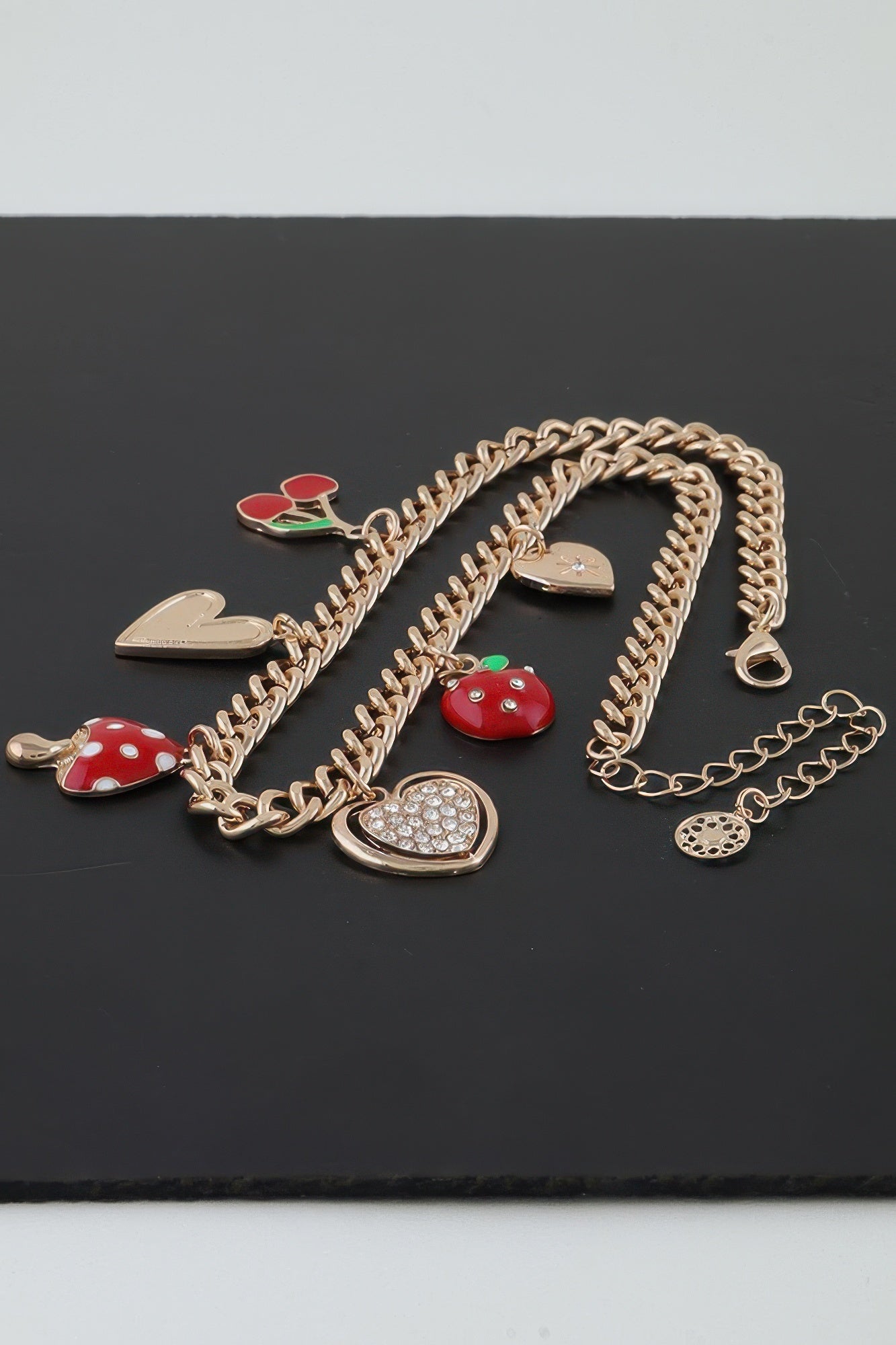 Gold charm chain necklace with red mushroom, hearts, and apple; links and clasp visible