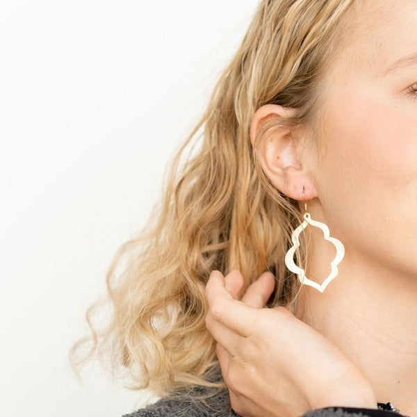 Gold quatrefoil drop earrings on model, showing openwork flower shape and hooks