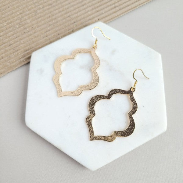 Gold quatrefoil drop earrings on white hex tile, openwork floral cutout design