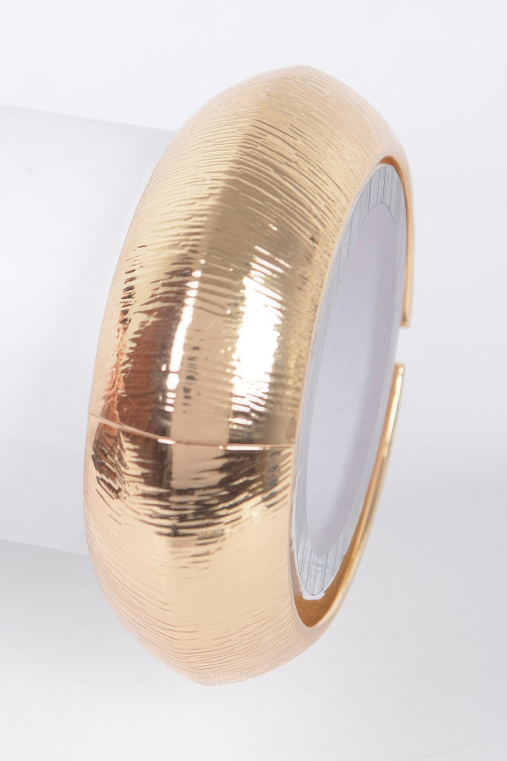 Gold textured metal bangle bracelet viewed from the side, glossy patterned surface