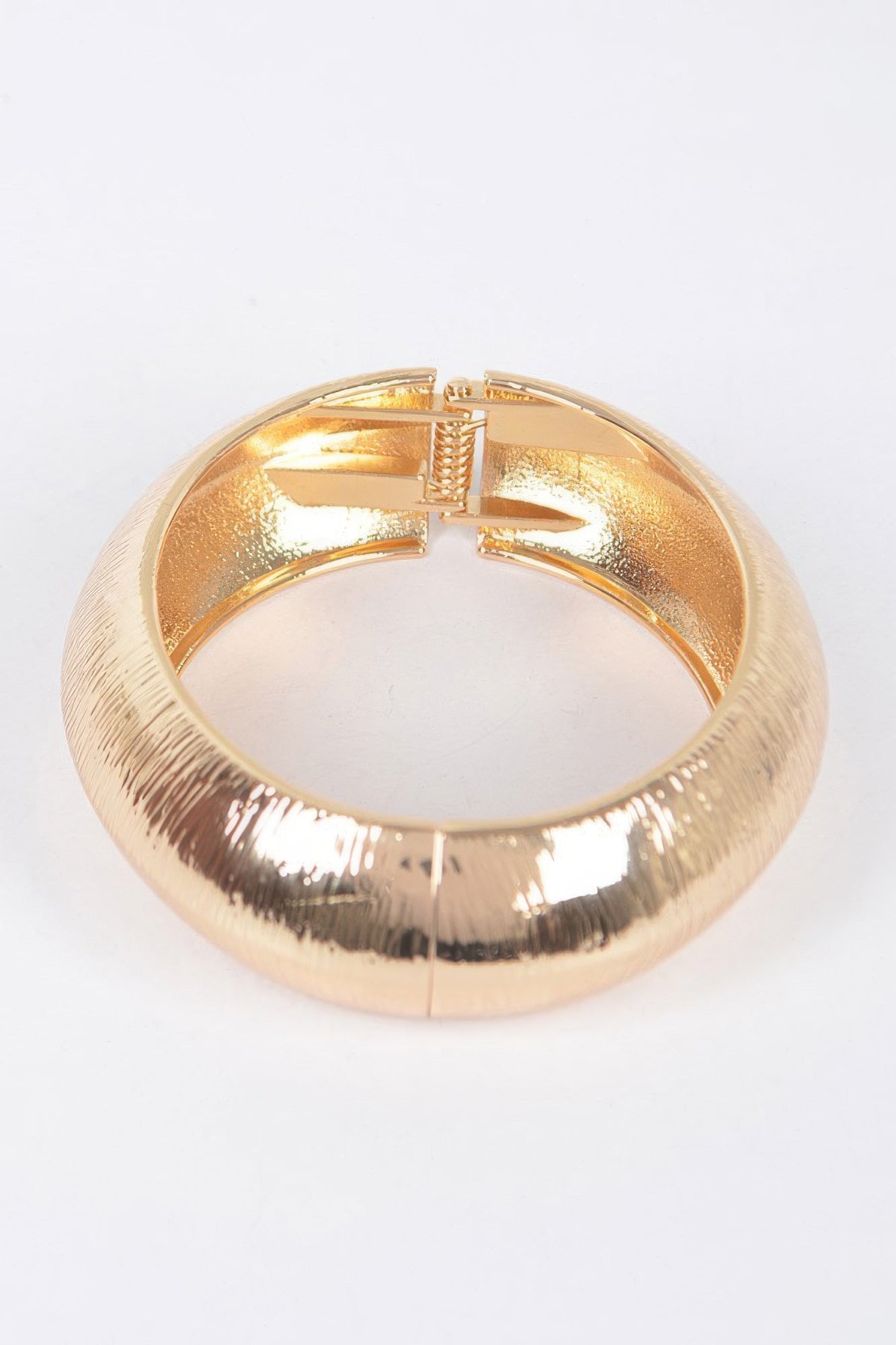 Gold textured metal bangle bracelet with clasp visible at the top center