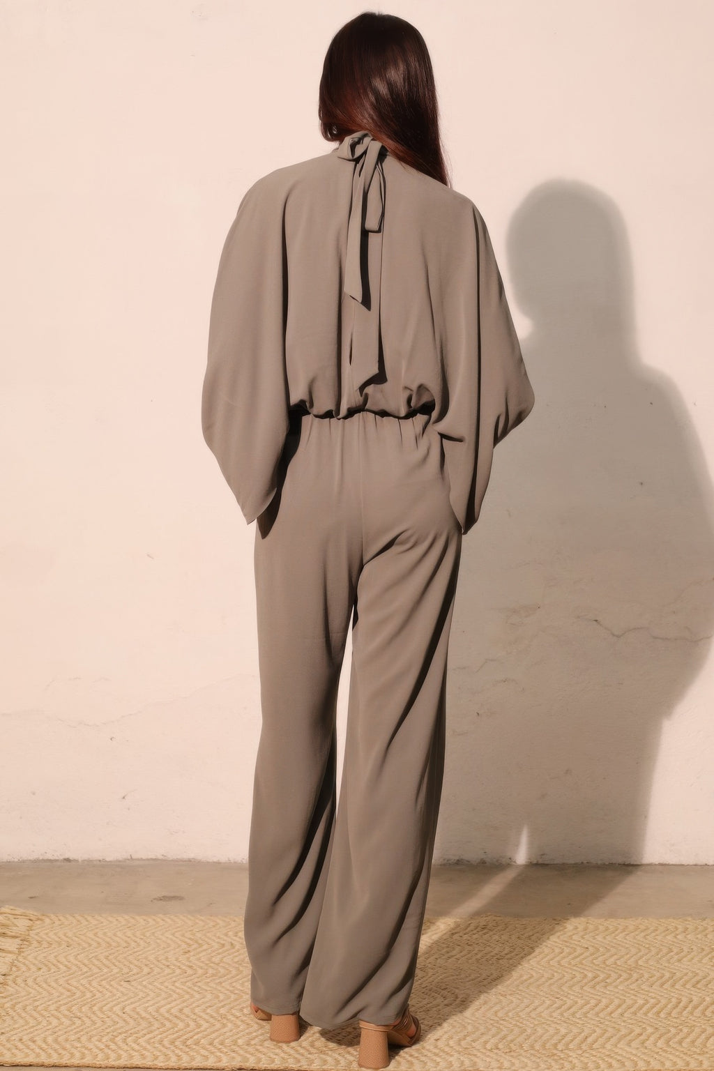 Back view of gray caftan jumpsuit with tie-neck detail and wide-leg silhouette