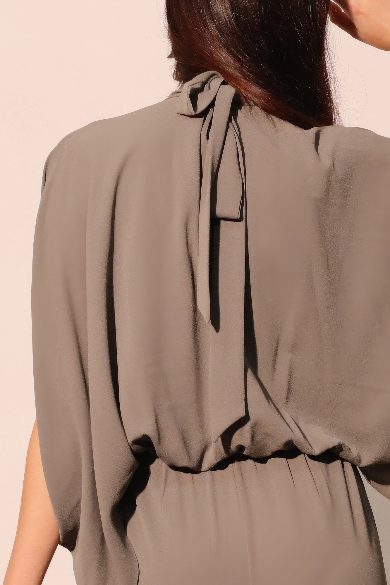 Close-up back of gray jumpsuit: bow-tie neck with gathered waist