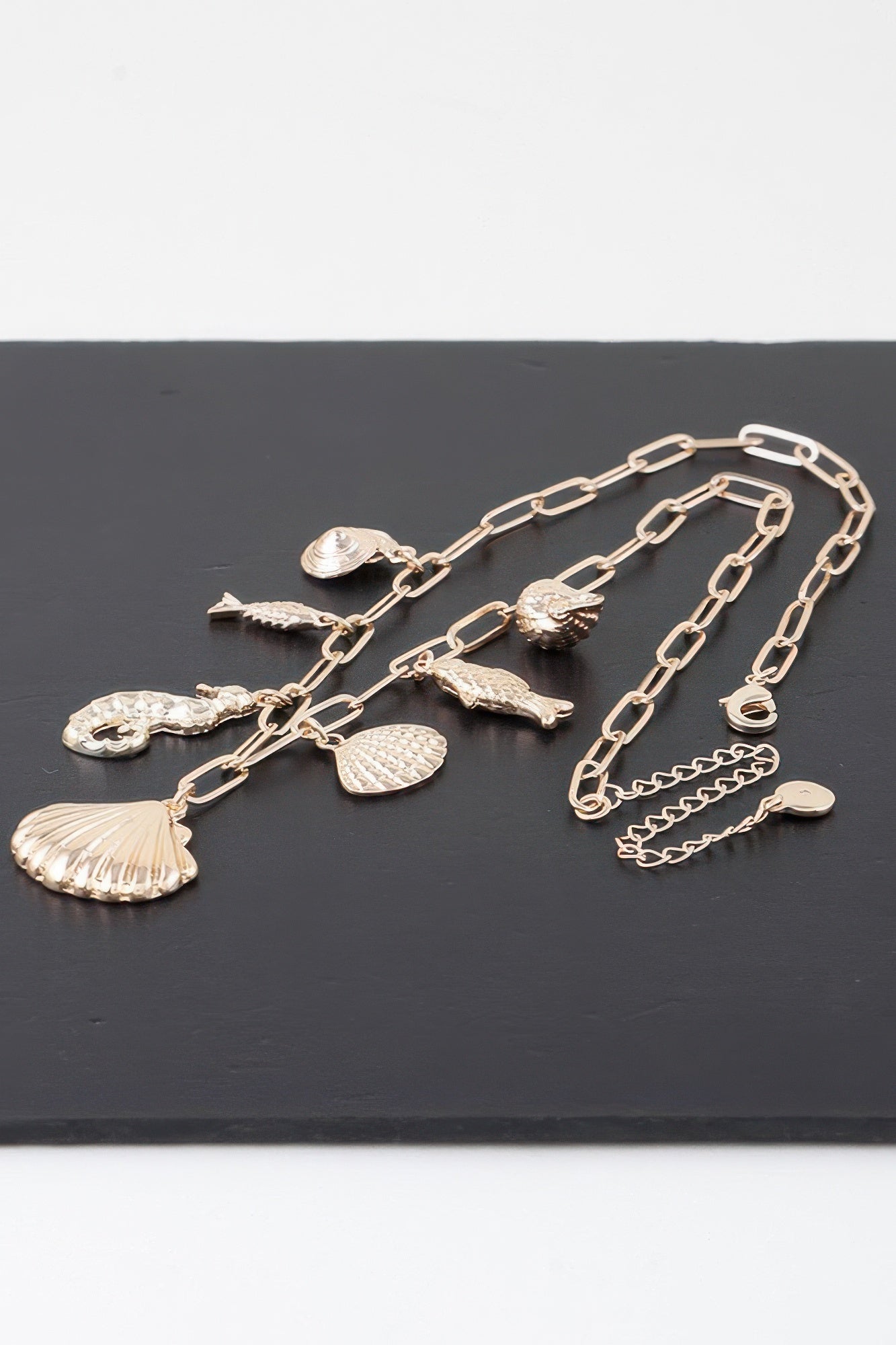 Gold necklace charms laid flat: shells, fish, and star-shaped pendants on chain