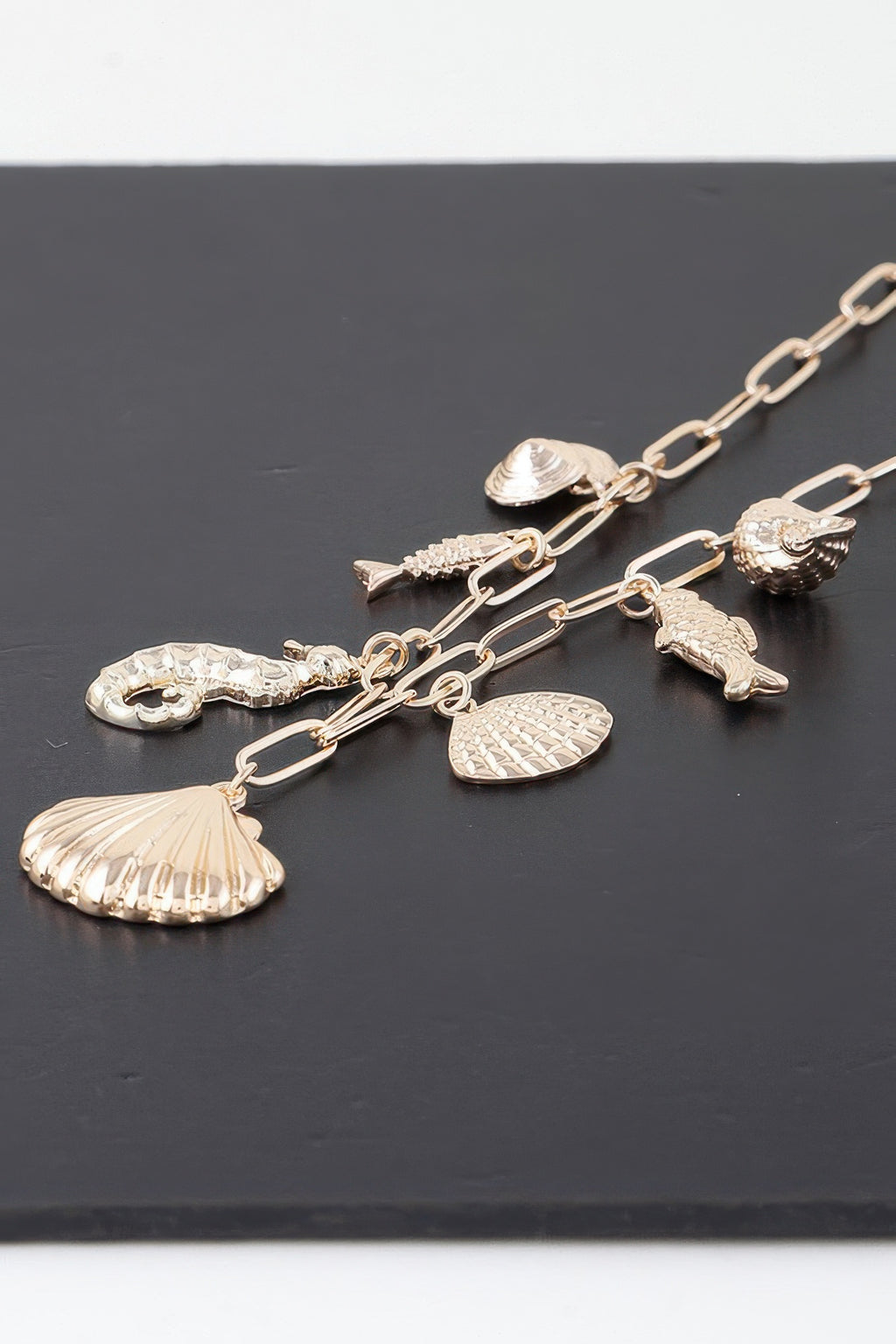 Gold charm chain close-up with seashell, fish, and scallop-like sea pendants