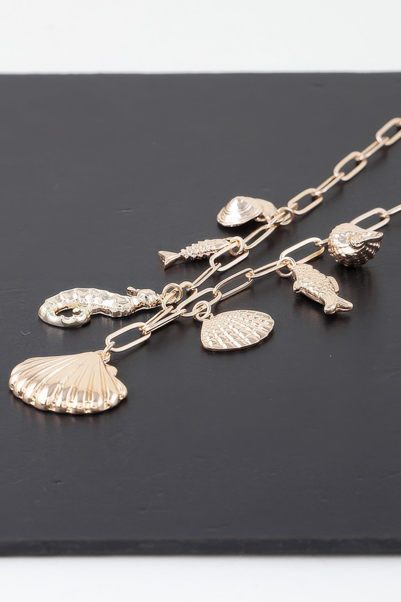 Gold charm chain close-up with seashell, fish, and scallop-like sea pendants