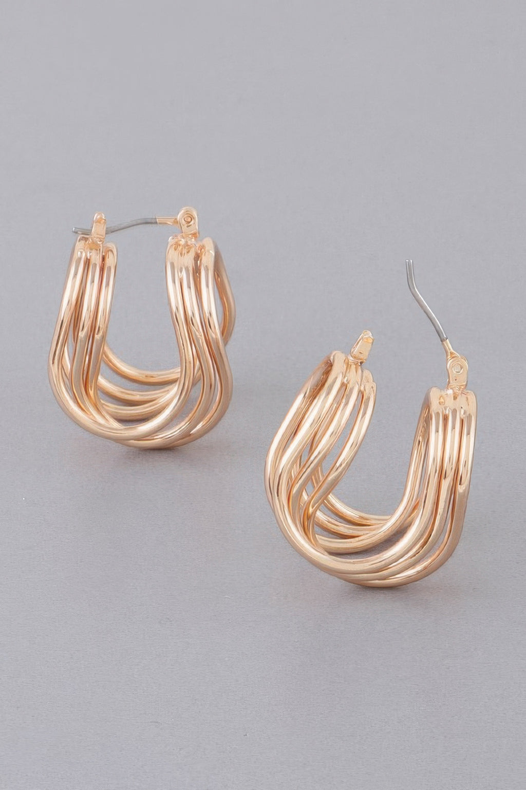 Triple shiny hoop earrings in gold tone, curved layered wire hoops, angled view