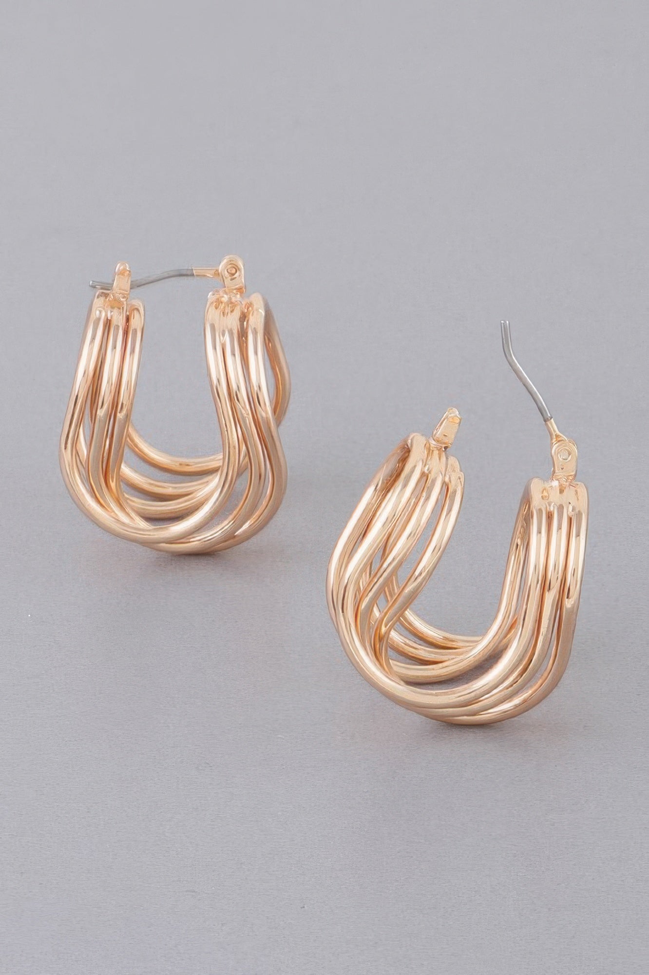 Triple shiny hoop earrings in gold tone, curved layered wire hoops, angled view