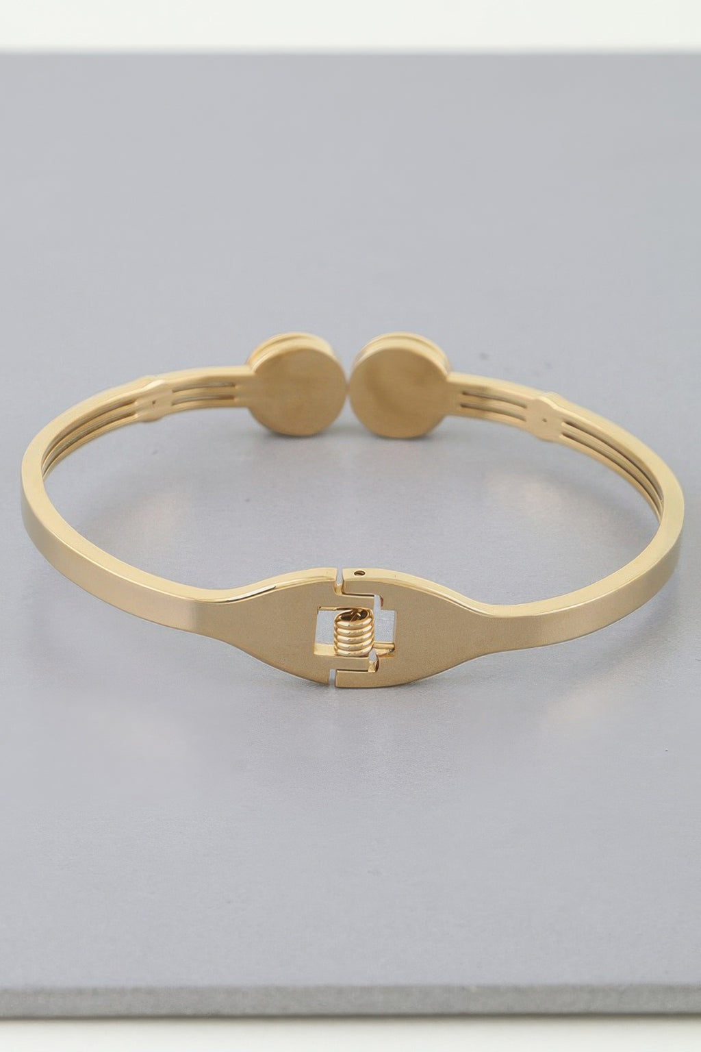Gold-tone wrap bracelet showing clasp and twin round clock charms on band