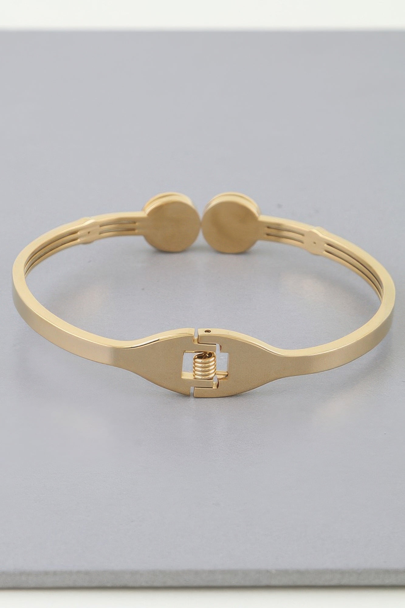 Gold-tone wrap bracelet showing clasp and twin round clock charms on band