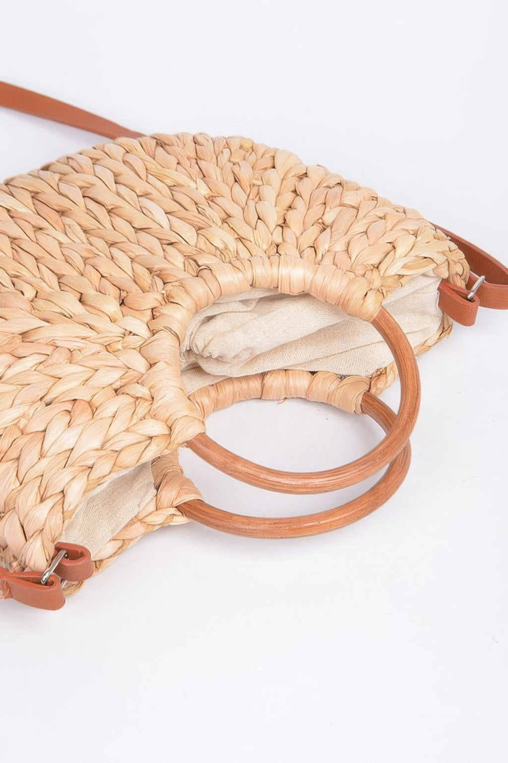 Close-up of Natural woven clutch with twist-knotted ring handles and tan strap clips.
