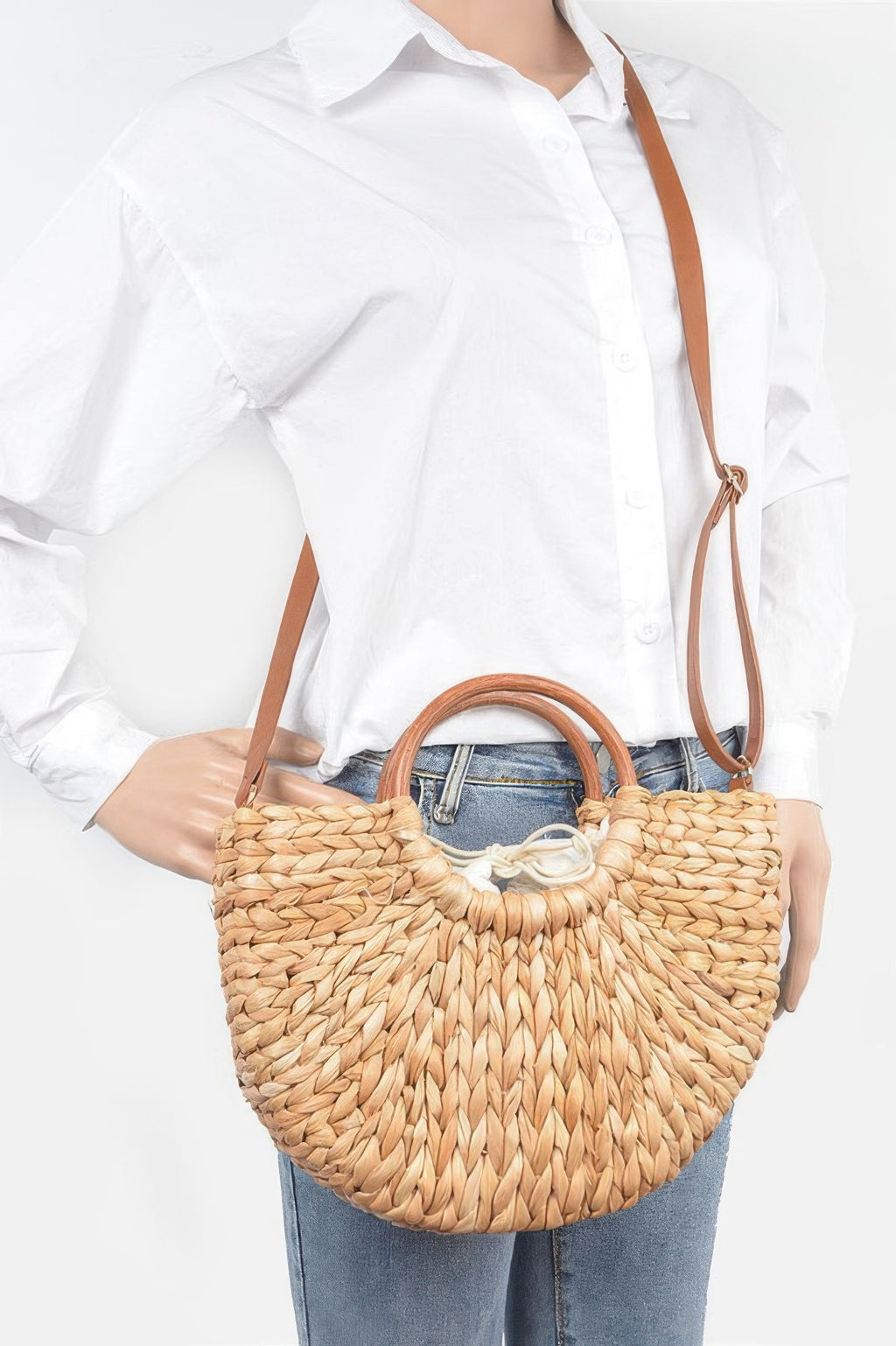 Natural woven clutch bag worn crossbody with twist-knotted top and tan strap.