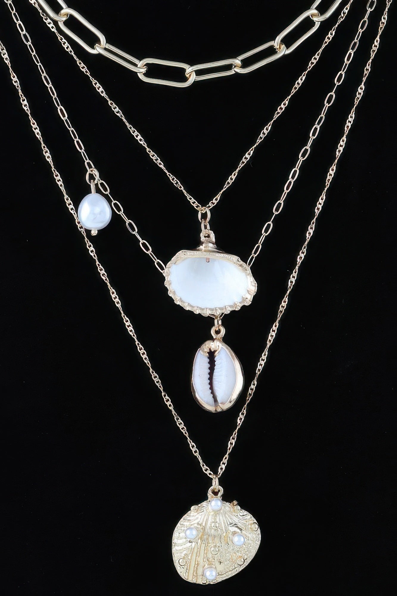 Gold-tone layered charm necklace with white shell charm, blue oval bead, and coin charm