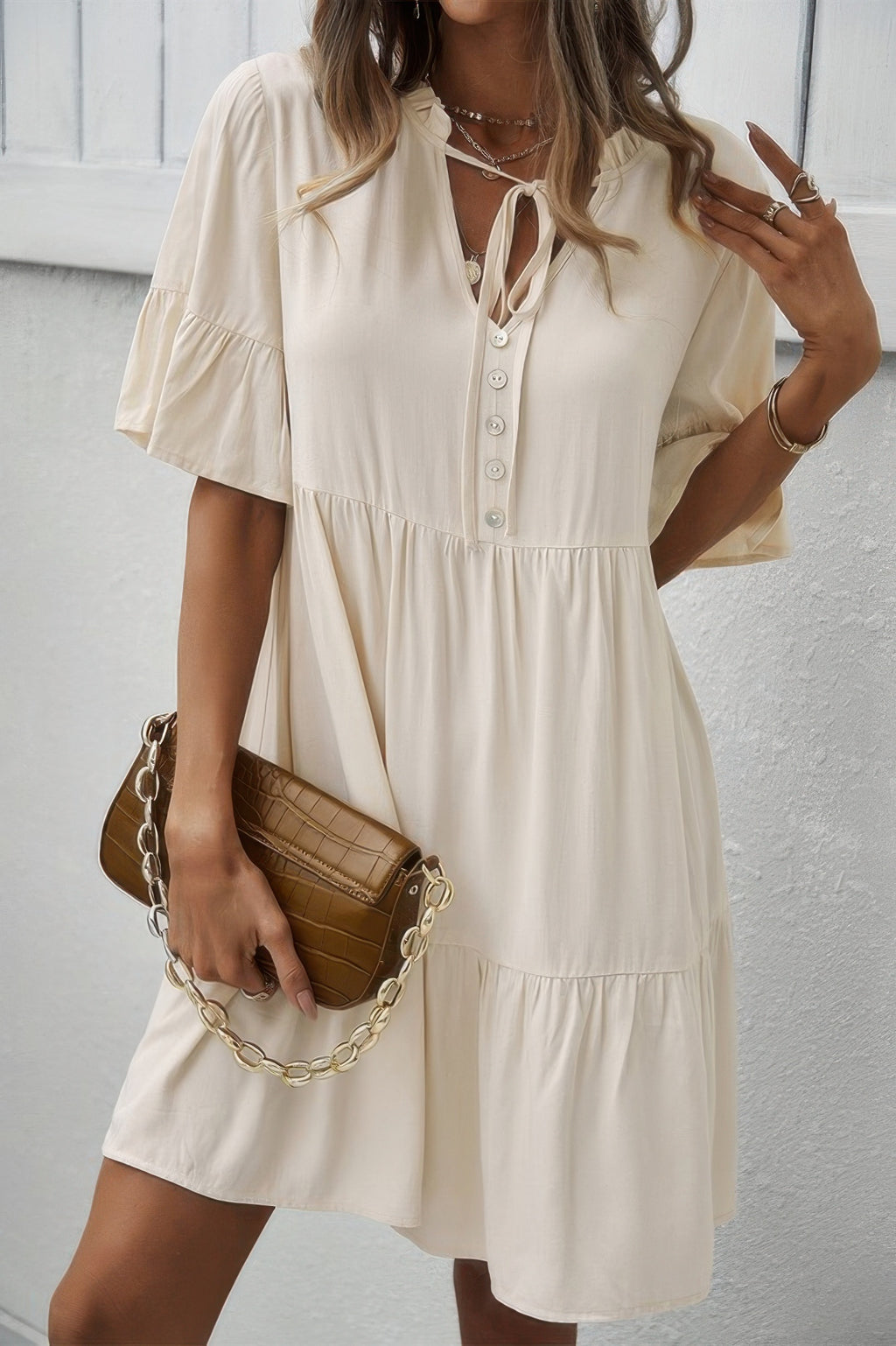 Cream V-neck button dress with tie detail, tiered ruffle hem, and short flounce sleeves.