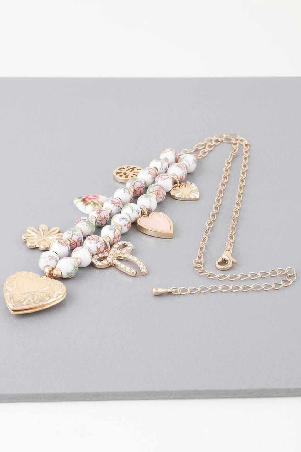 Heart charms necklace flat lay: pink-white beads with gold hearts, bow, and ribbon charms