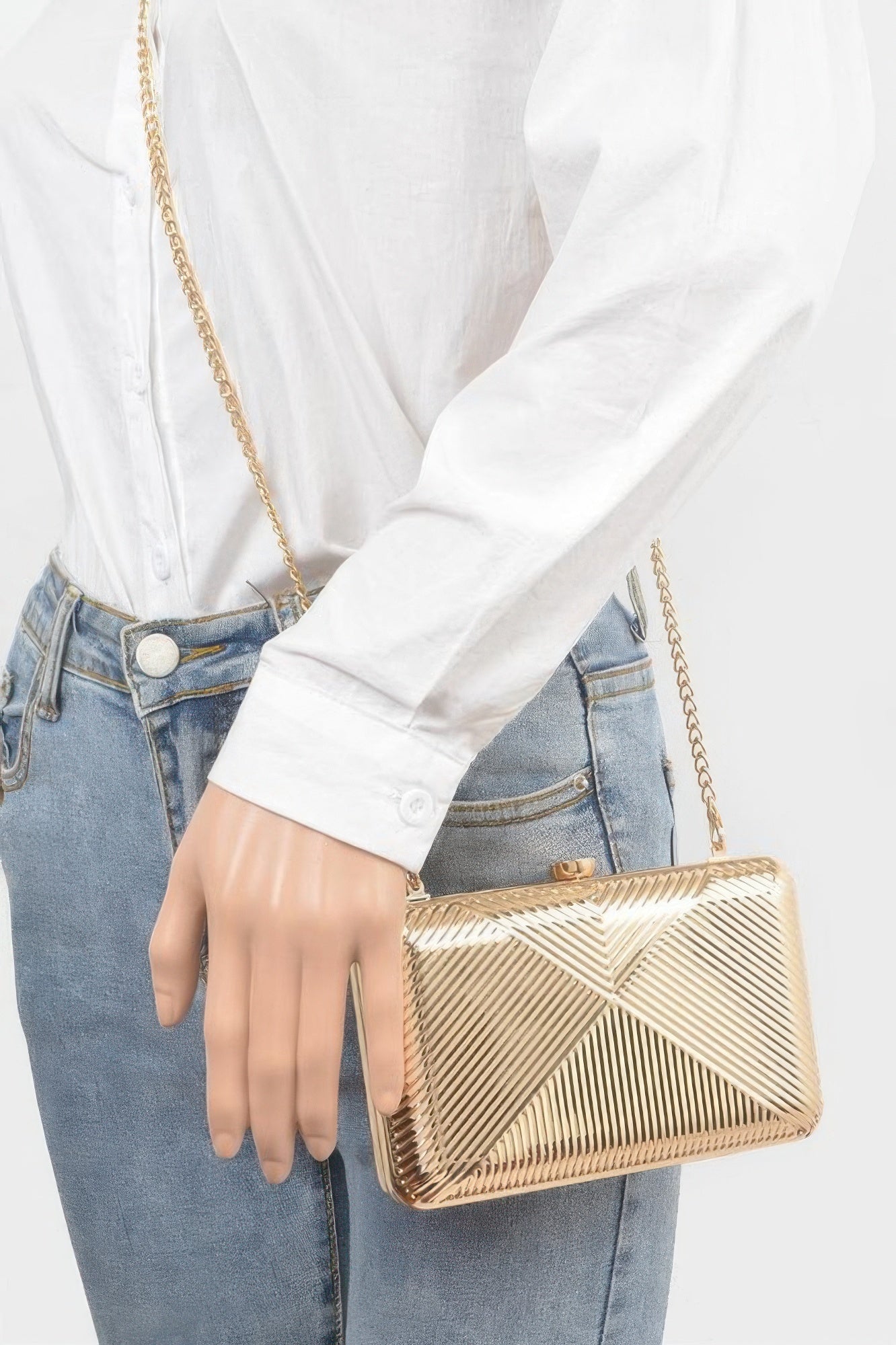 Gold metal clutch with long chain strap, held in hand