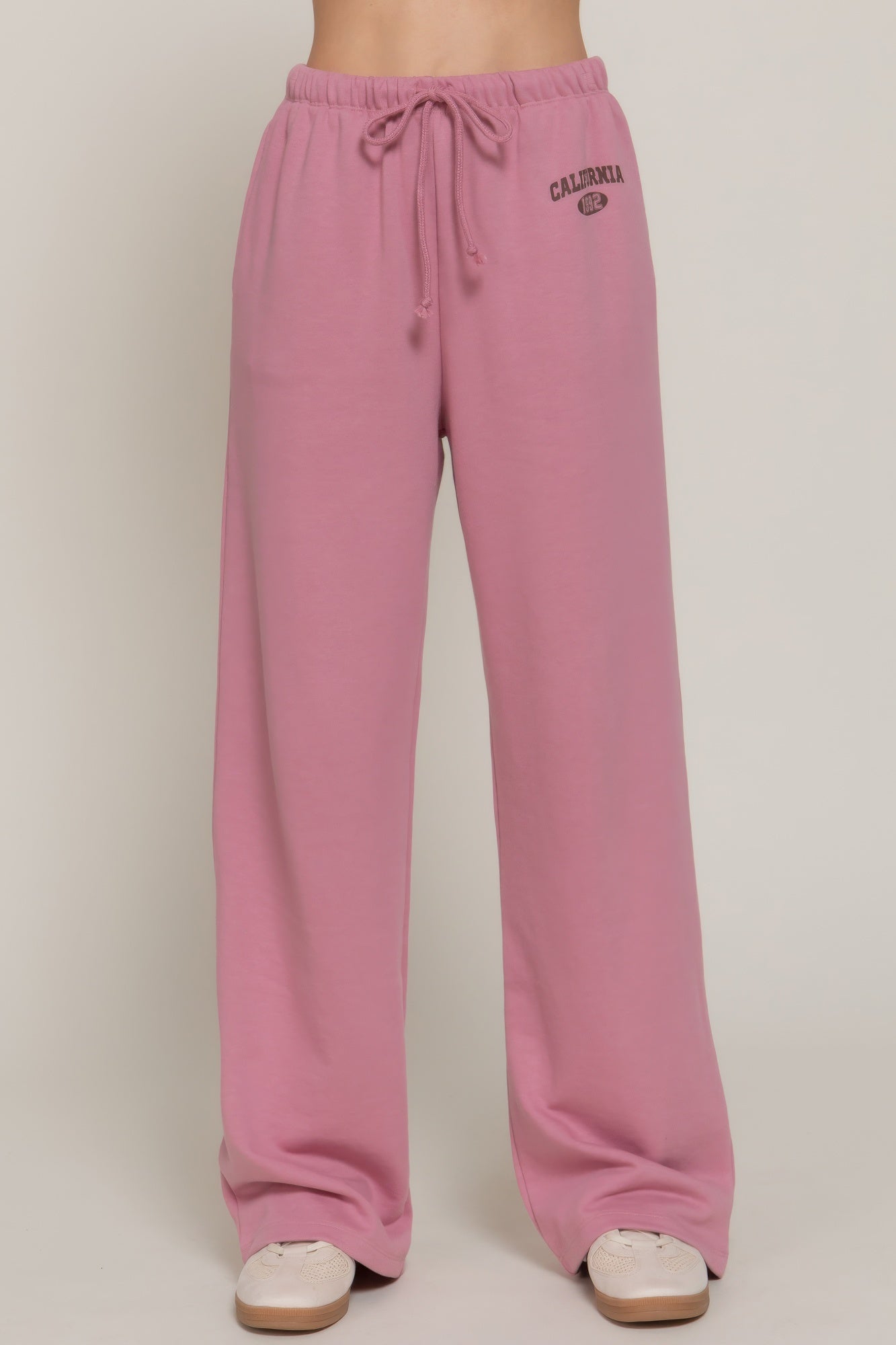Dusty pink sweatpants with drawstring waist and small “CALIFORNIA” logo detail on thigh