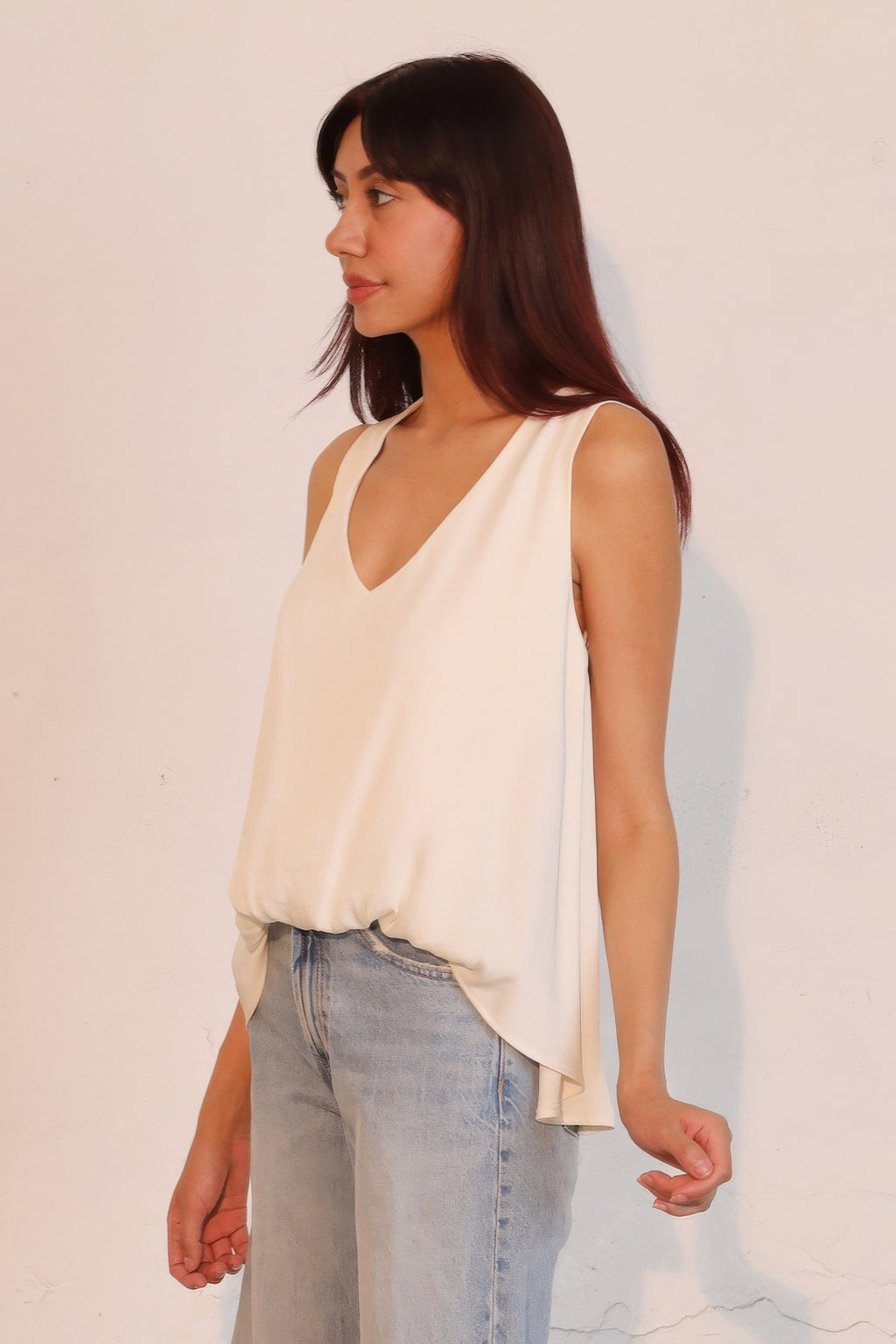 Washed poly silk front tucked top, ivory sleeveless V-neck with flutter hem, side view