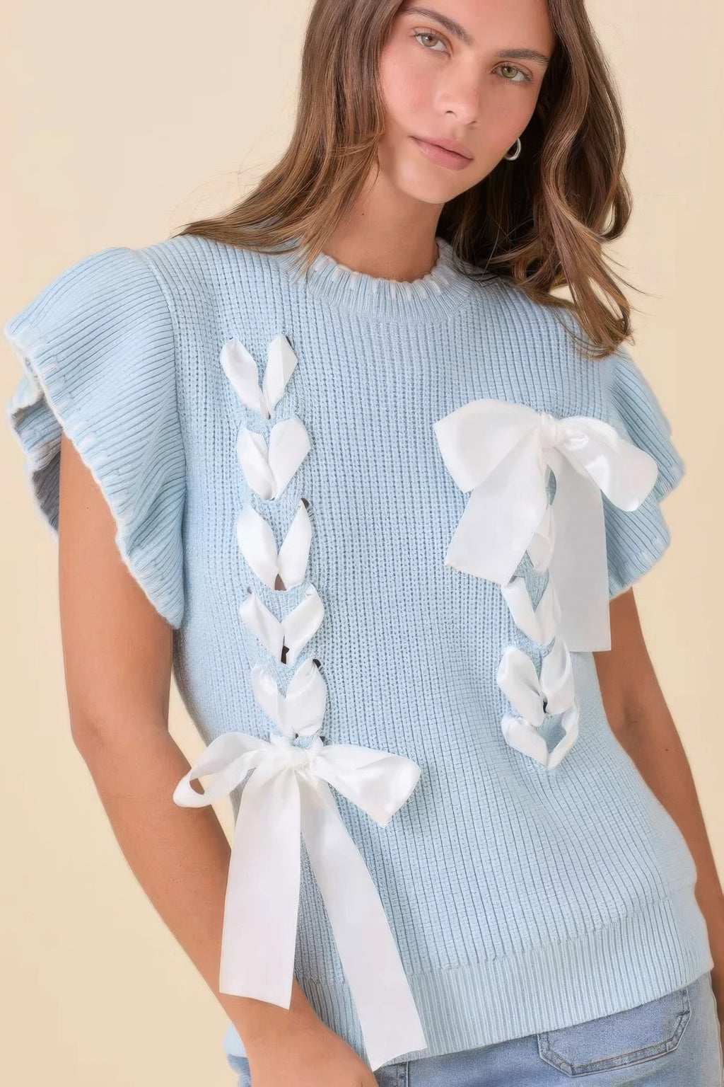 Close-up light blue sweater knit top with white ribbon bow appliqués