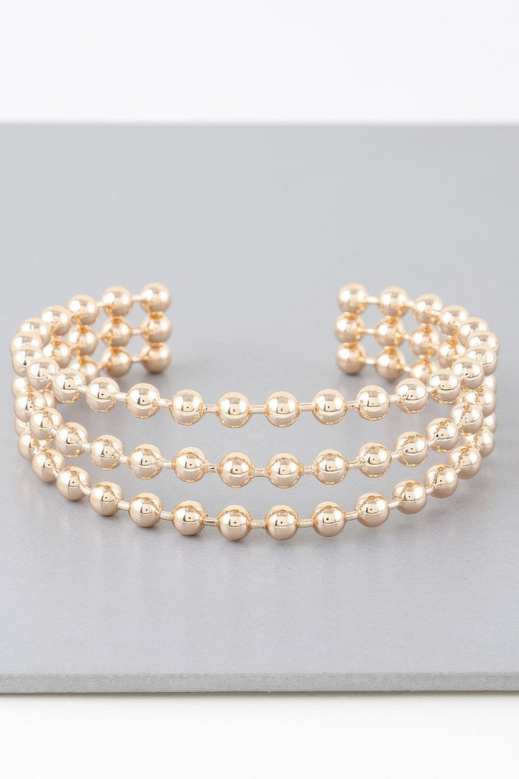 Wide cuff bracelet with triple rows of shiny gold round beads, openwork ends