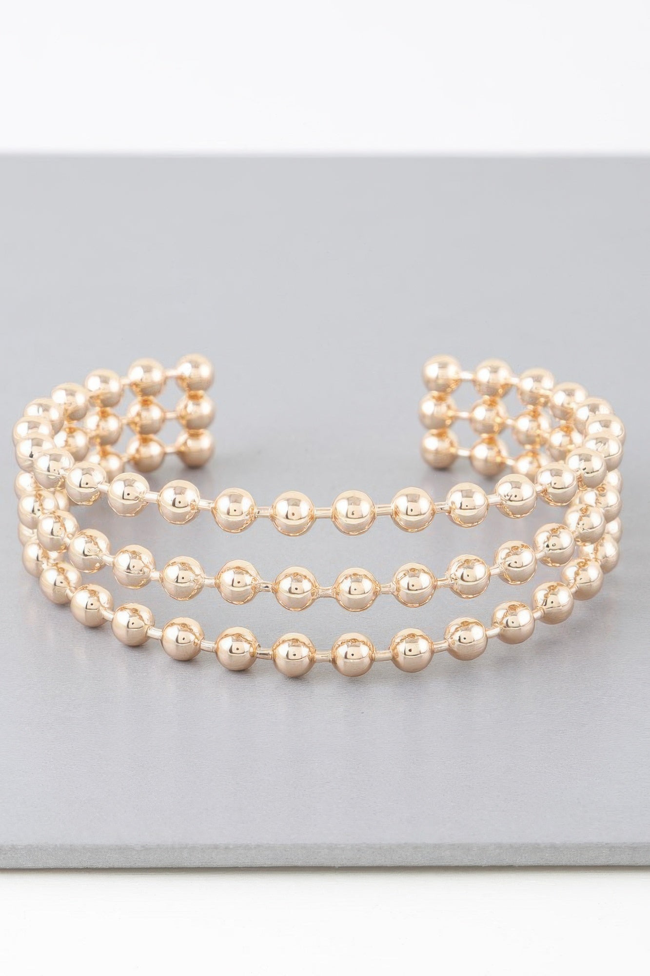 Wide cuff bracelet with triple rows of shiny gold round beads, openwork ends