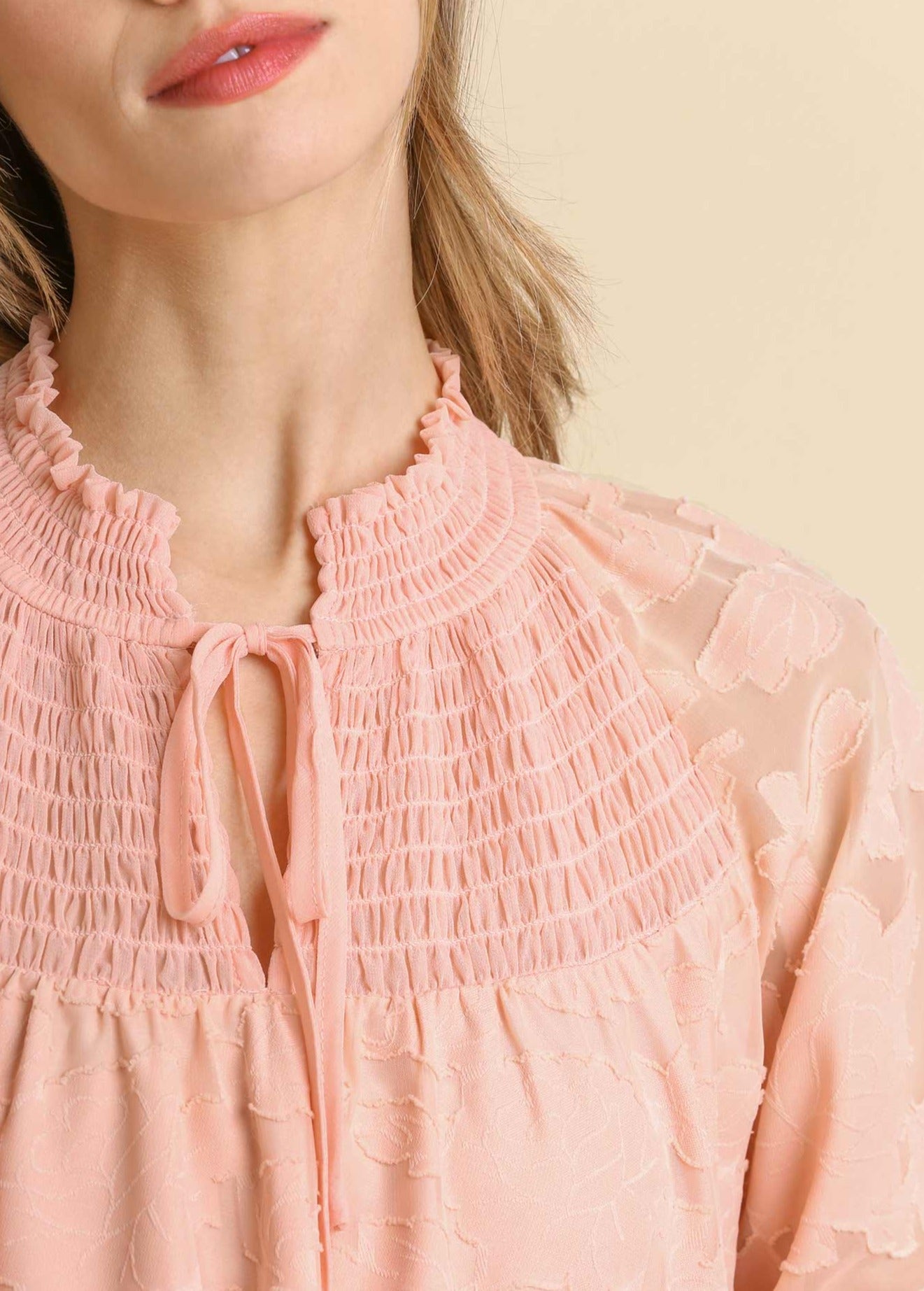 Close-up: blush smocked tie-neck yoke with jacquard texture and bow